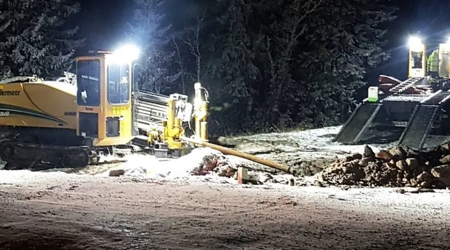 Borrigg i arbete en vinterkväll under arbetsbelysning. Borrstängerna går snett ned i marken vid startgropen, bredvid uppgrävda massor.
