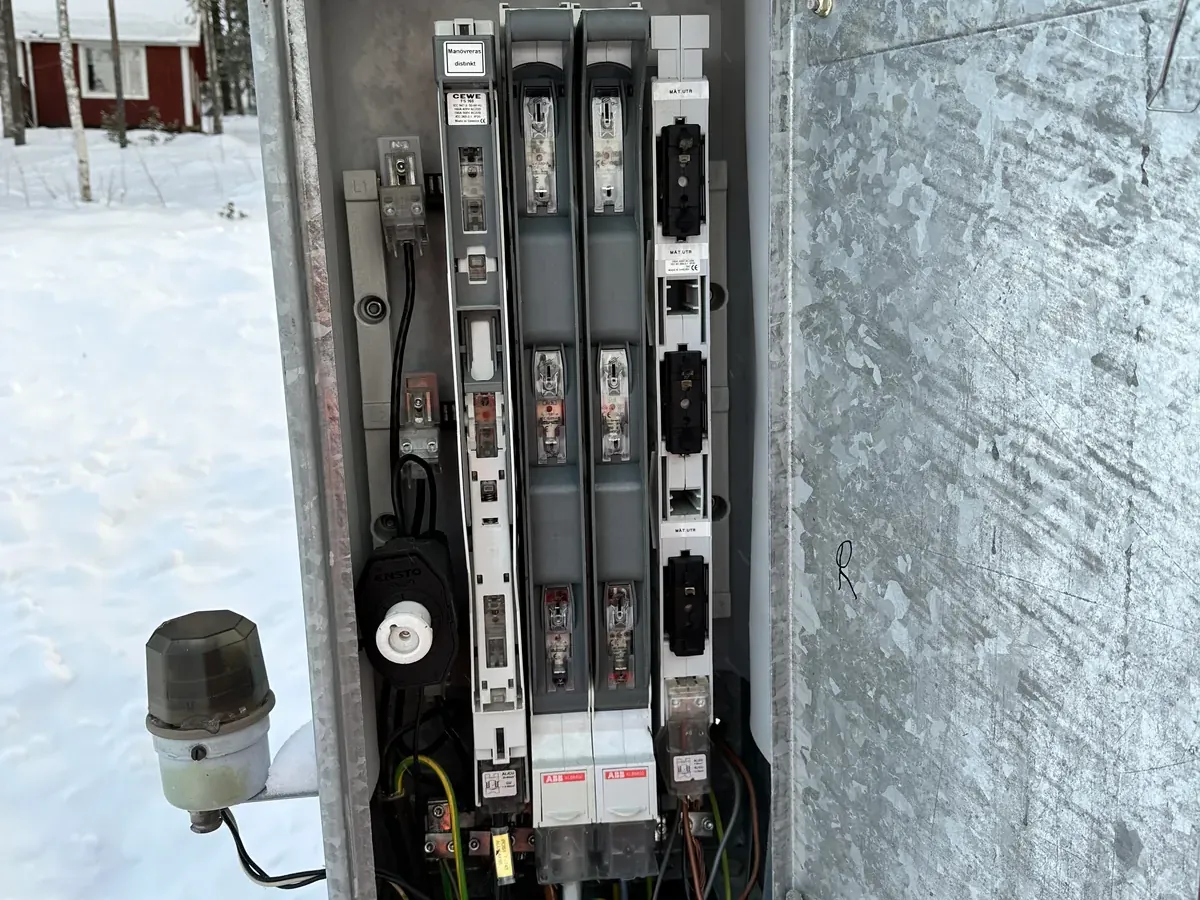 Öppet kabelskåp med säkringslastbrytare och kabelanslutningar, i snö.