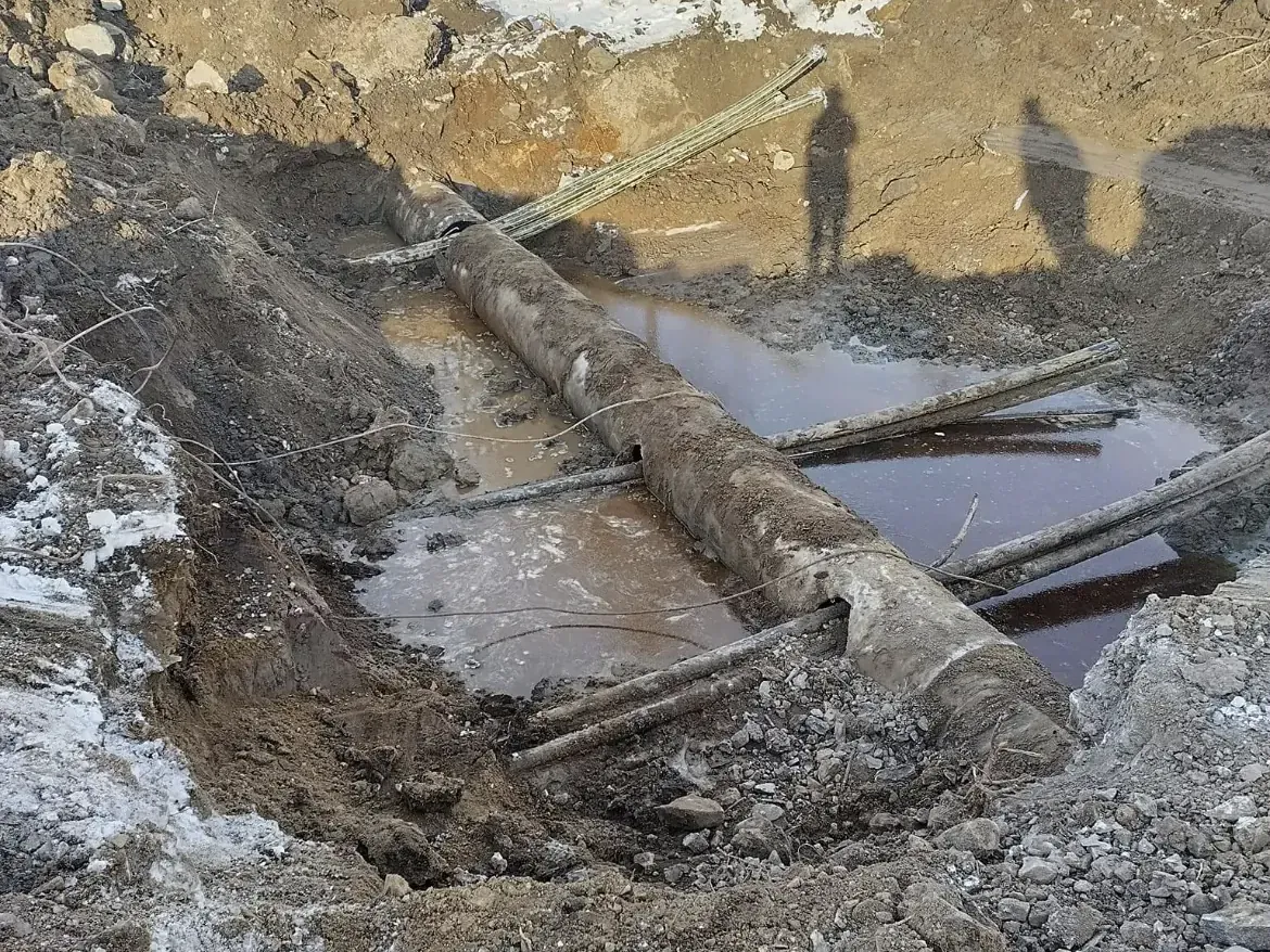 Vattenfylld schaktgrop där en befintlig ledning har frilagts för reparation.